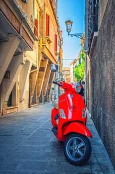 Chioggia, Italy, September 16, 2019: red scooter motorbike Vespa in narrow italian street in historical town centre, vertical view, Veneto Region