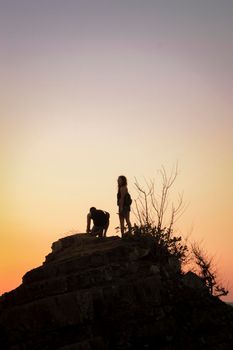 Boy and girl on a rock watching the sunset, silhouettes of couple watching the sunset