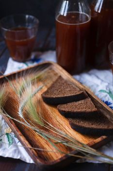 Slices of rye bread and rye spikelets on wooden plate with a bottle and a glass of kvass - the product of rye bread fermentation, traditional russian beverage, selective focus