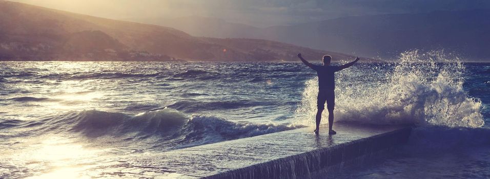 Feeling of freedom concept. Man standing on pier facing to the sea with big waves.