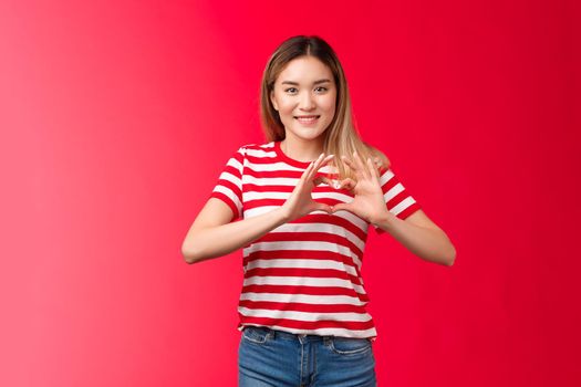 Asian girl express love and support lgbtq community. Heartwarming sweet tender blond female show heart sign near chest smiling friendly happily showing romantic attitude cherish relationship.