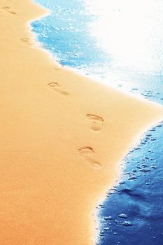 Detail of human feet in the golden sand at the beach. Summer travel and vacation concept.
