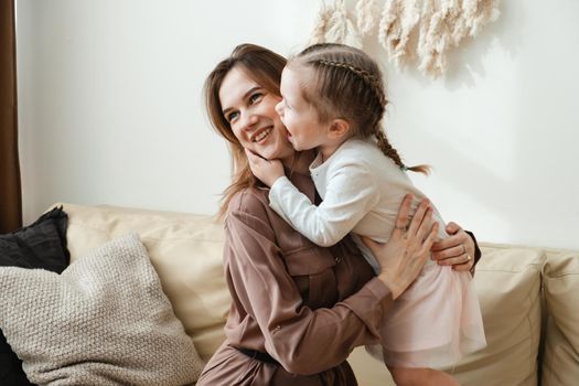 Lovely portrait of mother and daughter. A little girl kisses, laughs and tickles her mother in a bright bedroom. Mothers Day.