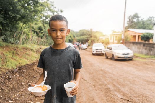 Nicaraguan boy holding a plate with nacatamal and a glass with coffee during a local celebration in the city of Rivas