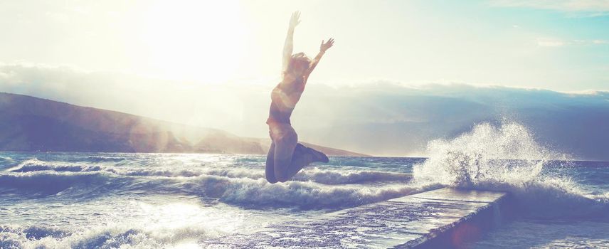 Feeling of freedom concept. Woman jump on pier facing to the sea with big waves.