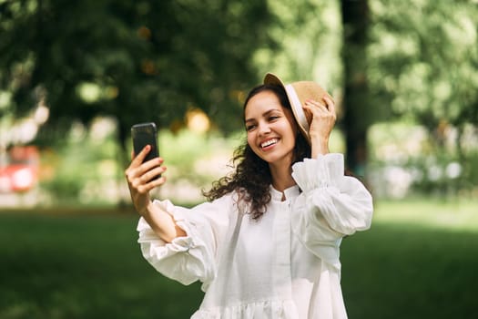 Young beautiful girl in a hat makes a selfie on her phone in the park. High quality photo