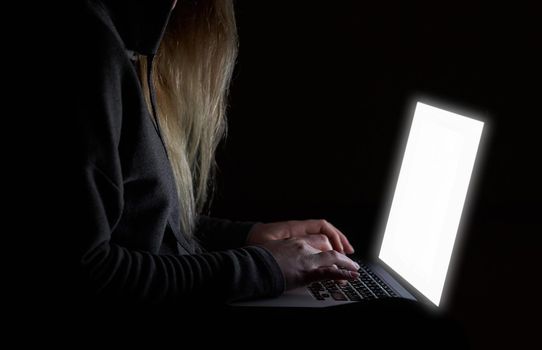 Overhead hacker in the hood working with laptop and mobile phone typing text in the darkroom. Russian hacker hacking the server in the dark. A hacker girl sitting in the dark with her laptop