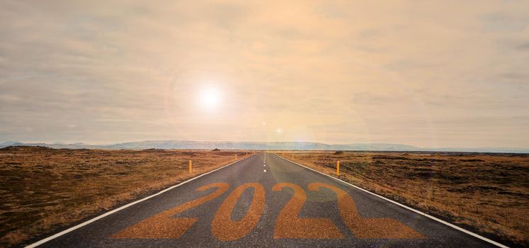 The word 2022 written on highway road in the middle of empty asphalt road at golden sunset and beautiful blue sky. Iceland. High-quality photo