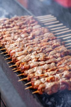 A lot of juicy meat kebabs in a row on the grill. Meat pieces strung on wooden skewers on the grill. The process of cooking kebabs with a lot of smoke. Cooking in nature