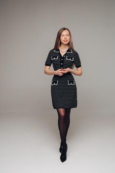 A beautiful woman in a black dress in the studio on a grey background.