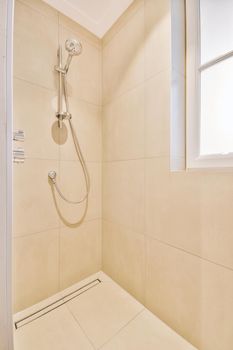 Shower faucets attached to tiled wall near glass partition and ornamental curtail in washroom at home