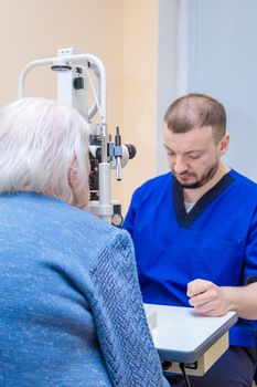 A male ophthalmologist checks the eyesight of an adult woman using a modern device with a light beam.