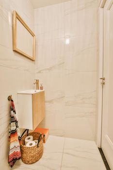 Cupboard with sink and mirror attached to tiled wall near door and drying rack in modern restroom