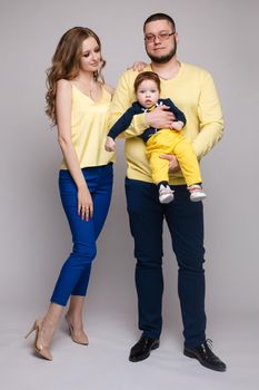 A beautiful family with a small child in the studio on a gray background