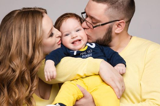 A beautiful family with a small child in the studio on a gray background