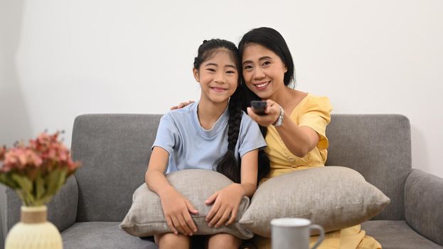 Mother and daughter sitting on sofa and watching tv. Family, children, love and happy people concept.