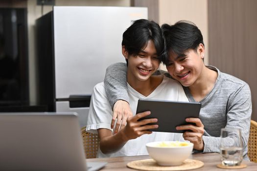 Young gay couple using digital tablet on bed at home, having fun checking social media applications together.