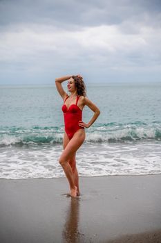 A beautiful and sexy brunette in a red swimsuit on a pebble beach, Running along the shore in the foam of the waves.