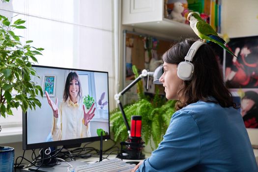 Online meeting of teenagers friends, guy with pet parrot sitting at home talking to a smiling female on computer monitor. Friendship, communication, technology, youth, lifestyle, young people concept