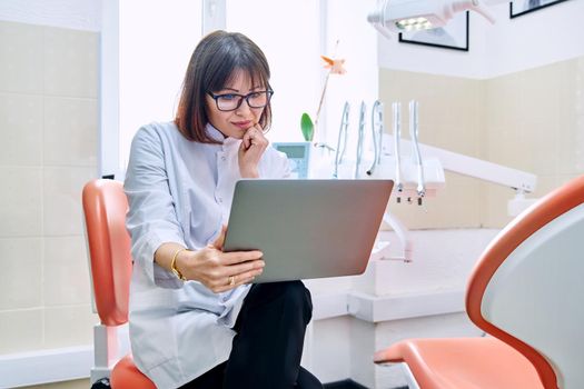 Online consultation, doctor help in clinic using laptop. Female dentist talking looking in laptop in dental office. Video conference, videocall, service, dentistry, medicine, technology concept