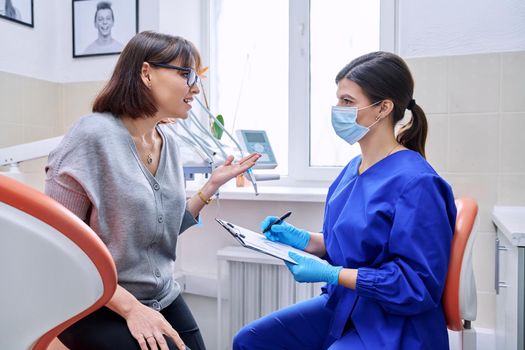 Dental office visit, female patient talking to doctor, dentist making notes for patient treatment. Treatment, dental care, prosthetics, orthodontics, dentistry concept