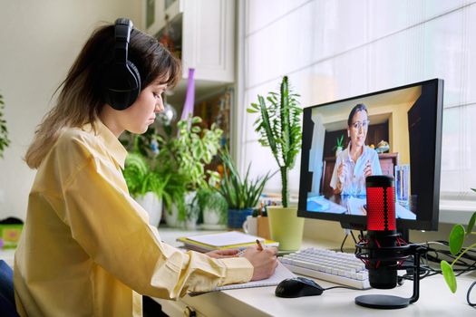 Teenage female student studying online at home, female in headphones with notebook talking to teacher by video, using computer. Chat call conference, e-learning college high school, technology concept