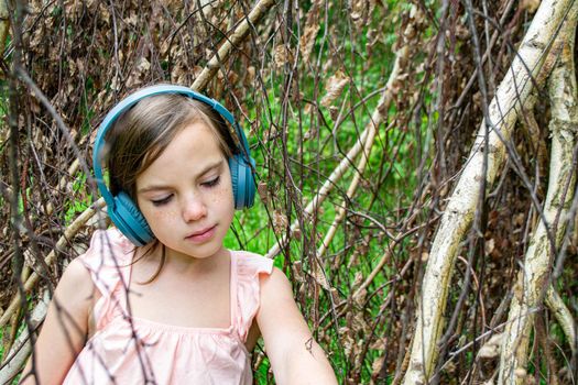 Young beautiful girl fooling around with a branch and wearing headphones on them to listen to music or block out sound due to auditory sensitivity. High quality photo