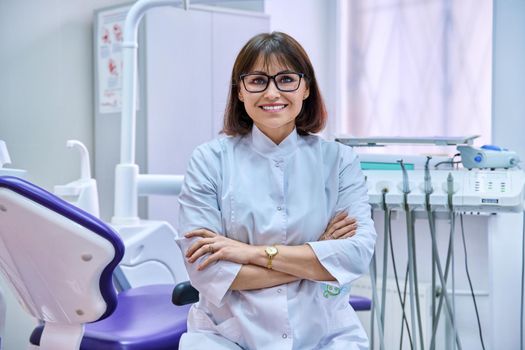 Portrait of confident female dentist in office looking at camera. Middle aged female doctor with crossed arms. Dentistry, medicine, health care, profession, stomatology concept
