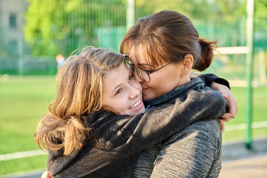 Portrait of happy mom and preteen daughter hugging together outdoor, near sports stadium, football field. Family, happiness, leisure, lifestyle, relationship, love, mother's day, motherhood concept