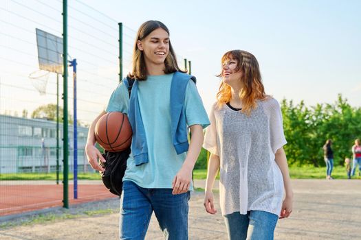 Young teenage male female students with backpacks ball walking outdoor near basketball playground court. Youth, active healthy lifestyle, education, college, high school, urban sport concept