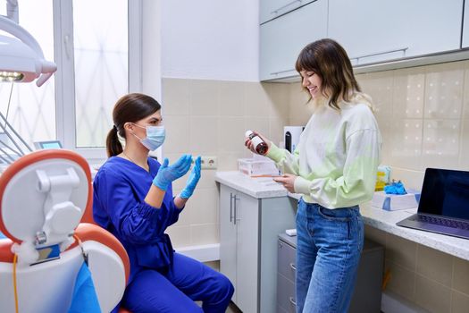 Dentist doctor showing telling giving medicine for teeth and oral cavity in bottle to young teenage female in office. Dentistry, health care, treatment, people, medicine concept