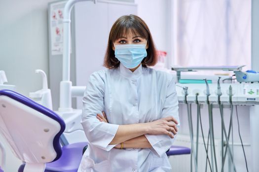 Portrait of confident female dentist doctor in office looking at camera. Middle aged female in medical protective mask. Dentistry, medicine, health care, profession, stomatology concept