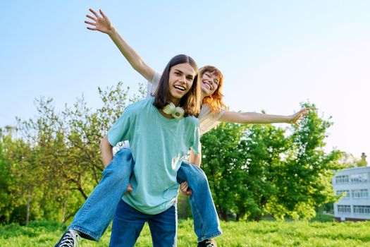 Couple of happy having fun teenagers together outdoor. Young teenage male and female laughing in park on lawn. Joy, happiness, friendship, summer, students, holidays, youth concept