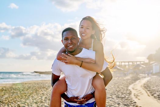 Happy young beautiful couple having fun on beach. Afro american asian couple laughing enjoying vacation in seaside nature. Multicultural, multiethnic family, relationships, togetherness, lifestyle