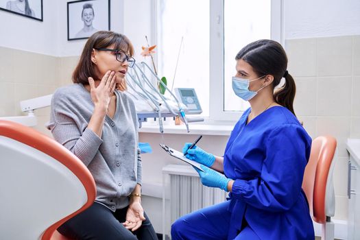 Dental office visit, female patient talking to doctor, dentist making notes for patient treatment. Treatment, dental care, prosthetics, orthodontics, dentistry concept