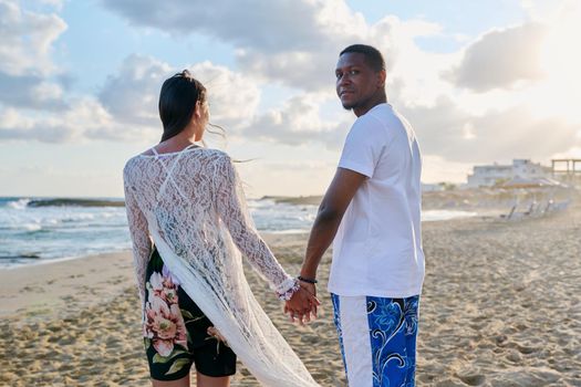 Young happy couple walking on the beach holding hands, back view. Honeymoon, dating, happiness, relationship, vacation, love, romance concept