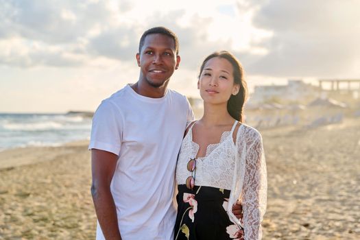 Young couple in love on the beach together. Multiethnic couple, asian woman and african american man. Love, honeymoon, relationship, lifestyle, togetherness, happiness, dating, multicultural family concept