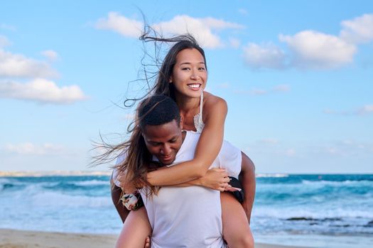 Happy young beautiful couple having fun on beach. Afro american asian couple laughing enjoying vacation in seaside nature. Multicultural, multiethnic family, relationships, togetherness, lifestyle