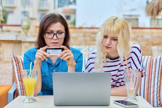 Mother and teenage daughter doing online shopping together using laptop and credit card. Family vacation, lifestyle, technology, shopping concept