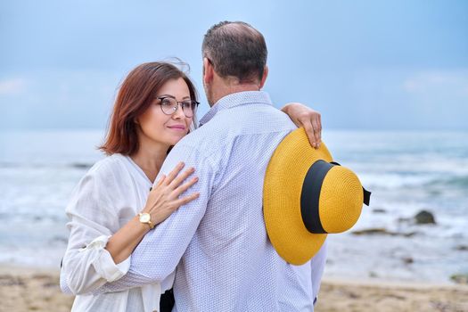 Portrait of happy hugging middle age couple, sea nature sky waves background. Age, relationship, love, leisure, vacation, people concept