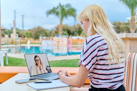 Remote online lesson on laptop screen, web chat with teacher, individual consultation of teenage. College high school student girl sitting at outdoor table, talking listening tutor on video conference