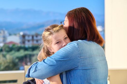 Mom hugging her preteen daughter. Girl schoolgirl with backpack hugging her mother on porch of house. Family, relationship, childhood, happiness, mother's day concept