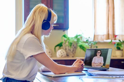 Teenage female student in headphones sitting at home using laptop talking to teacher, studying online remotely. E-learning, videocall, virtual lessons, knowledge, technology in education concept