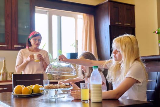 Children two sisters eating at home in the kitchen, teenage and preteen girls having breakfast together, mother cooking. Family, people, children, food, lifestyle concept