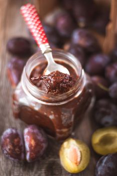 plum jam in glass jar with spoon on wooden background. High quality photo