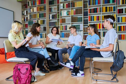 Group of teenagers with middle aged female teacher at library, sitting talking discussing. Education, lesson, youth, teaching, high school, teamwork, college concept.