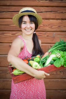 happy young girl holding harvest of vegetables next to wooden background. High quality photo