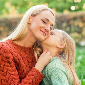 Cute daughter kisses her young mother while sitting at the park