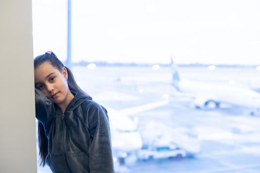 little baby girl waiting boarding to her flight in airport transit hall and looking at airplane parking near departure gate. Travelling by air with child.