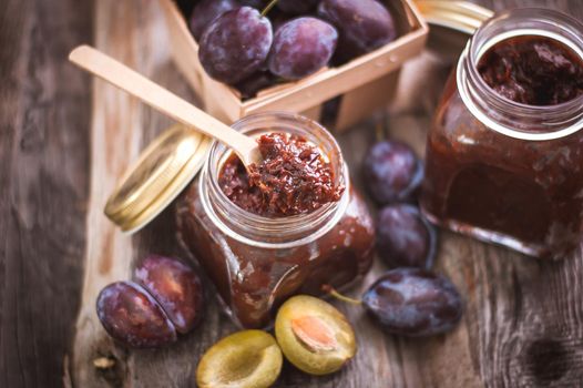 plum jam in glass jar with spoon on wooden background. High quality photo